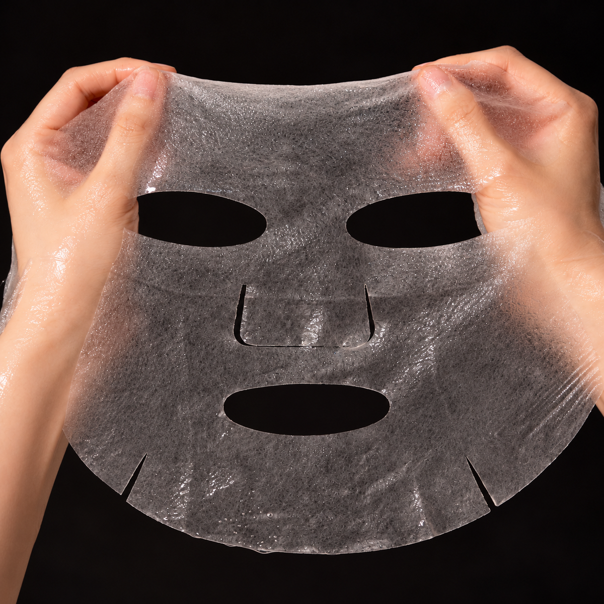 Unfolded FAU Collagen Velvet Mask held between two hands, showing the wet sheet texture and face-shaped openings.